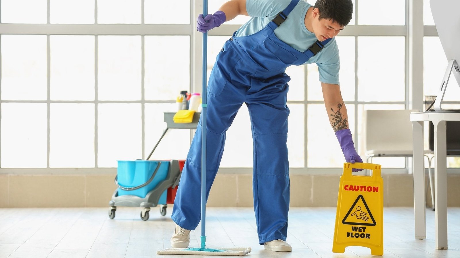 Cleaner in blue overalls mopping a bright floor